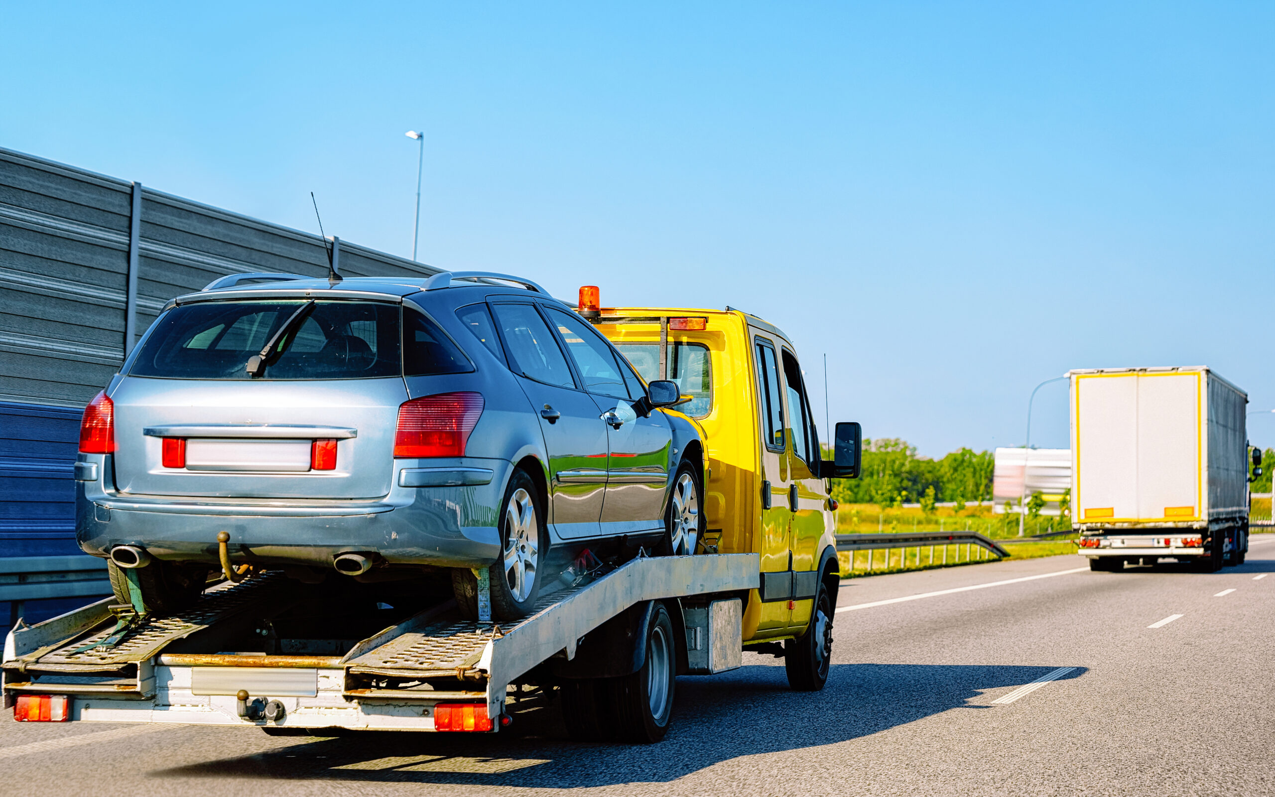 Low tow truck trailer with car in road. Auto vehicle with Carrier transporter hauler on driveway. European transport logistics at haulage work transportation. Haul on highway.